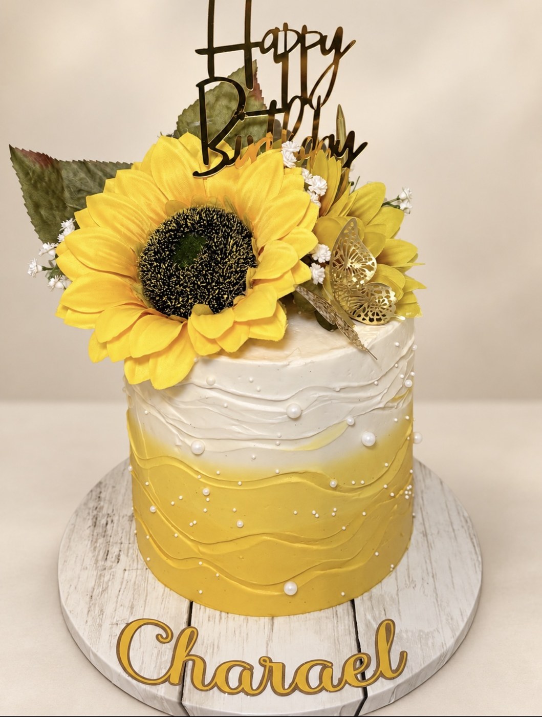 Yellow and white celebration cake with a sunflower and gold birthday topper