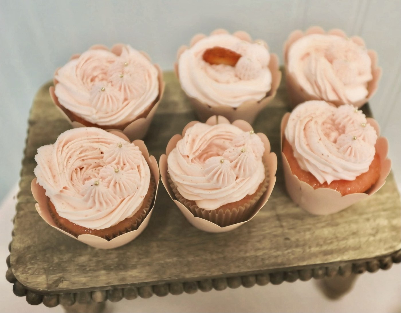 Six blush pink cupcakes with piped floral frosting on a gold stand