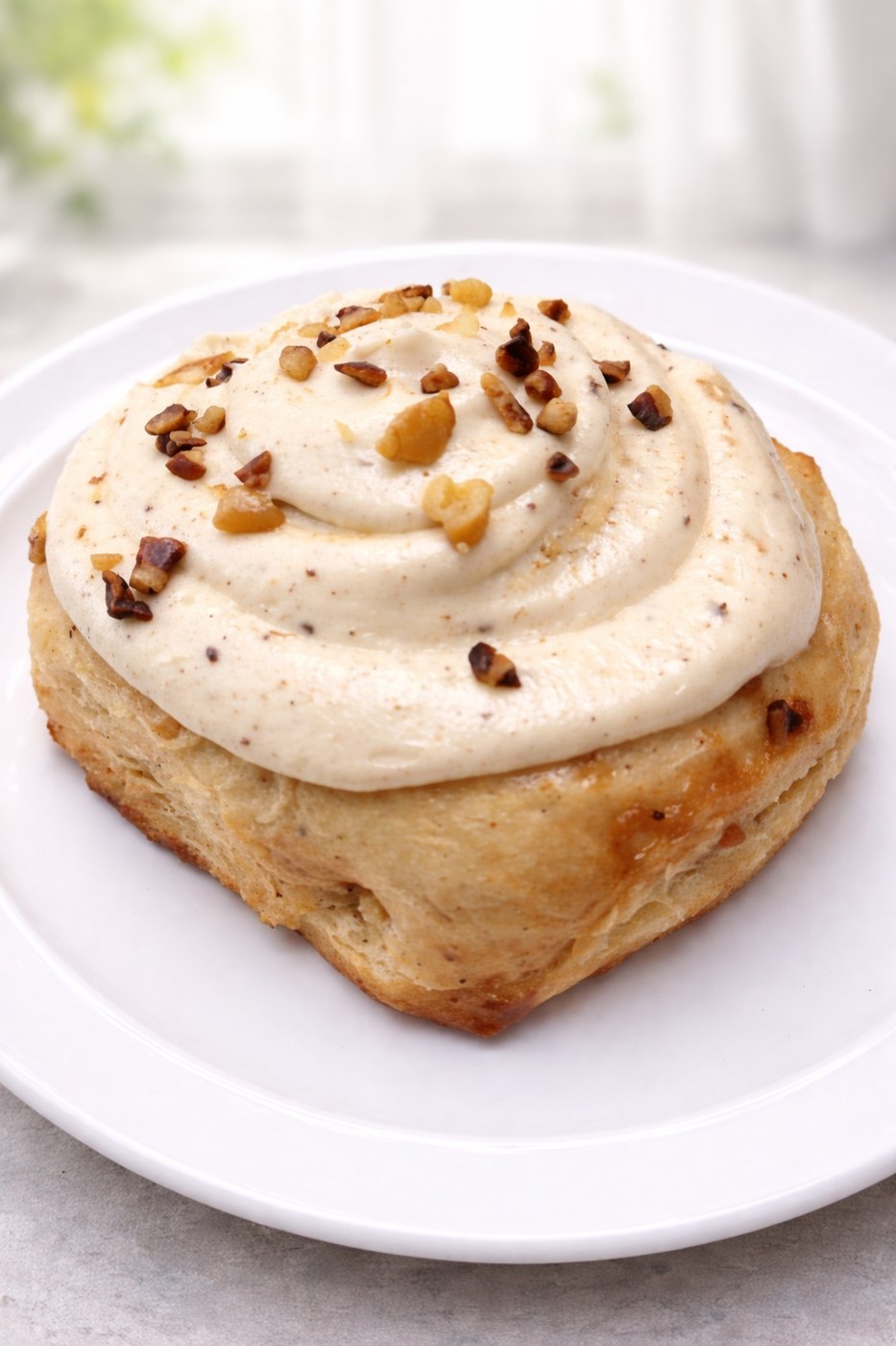 Frosted cinnamon roll with chopped nuts on a white plate